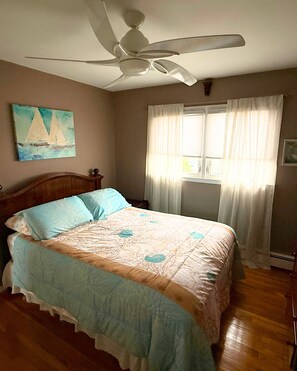 A bedroom with a bed, a ceiling fan, a window with curtains, and a painting on the wall. - Peaceful Canal-Front 1 bedroom Retreat Near Hospitals, LIRR & Beaches (Lindenhurst)