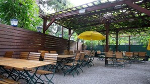 Un área de patio al aire libre con mesas y sillas de madera, un paraguas amarillo y una estructura de pérgola de madera.