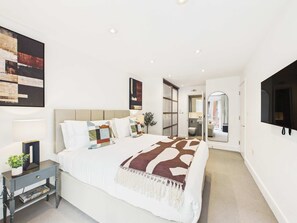 Une chambre à coucher moderne avec un lit, des tables de chevet, un miroir et un téléviseur.
