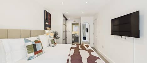 Une chambre à coucher moderne, avec un lit, un téléviseur fixé au mur et un couloir menant à la salle de bain.