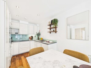 A modern kitchen with white cabinets, a marble countertop, and a dining area with a white table and chairs. - Comfy 2 Bedroom Westminster Apartment (Greater London)