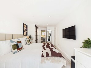 Een moderne slaapkamer met een bed, een televisie en een badkamer door een open deur zichtbaar.
