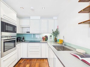 A modern kitchen with white cabinetry, a built-in oven, a coffee maker, and a plant on the counter. - Comfy 2 Bedroom Westminster Apartment (Greater London)