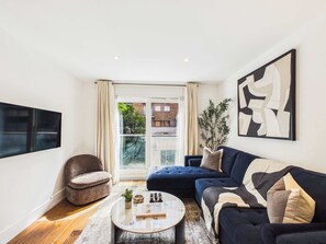 A modern living room with a sofa, armchair, coffee table, and artwork. - Comfy 2 Bedroom Westminster Apartment (Greater London)