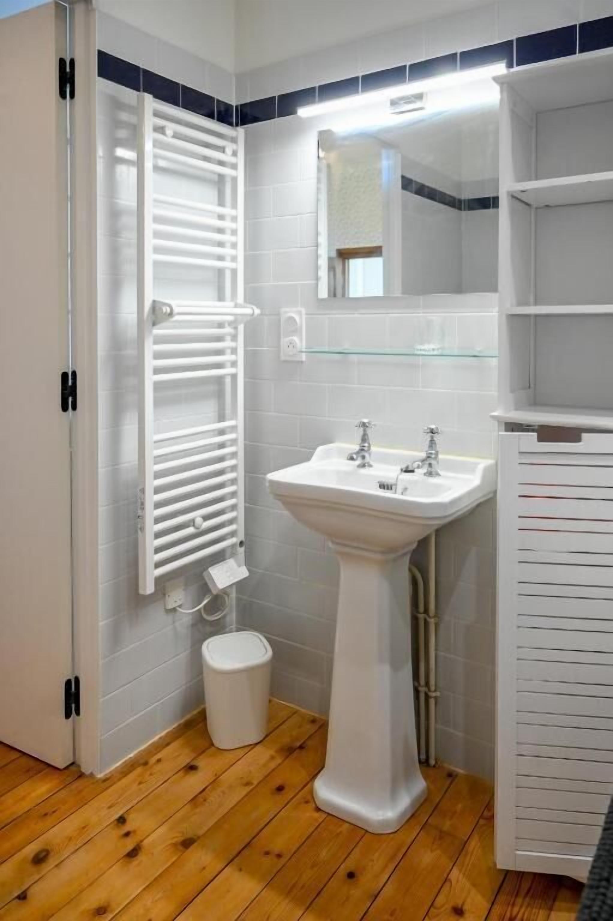 A bathroom with a pedestal sink, a towel rack, a mirror, and a glass shelf.