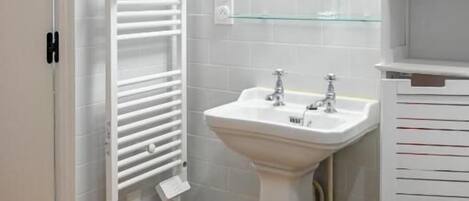A bathroom with a pedestal sink, a towel rack, a mirror, and a glass shelf.