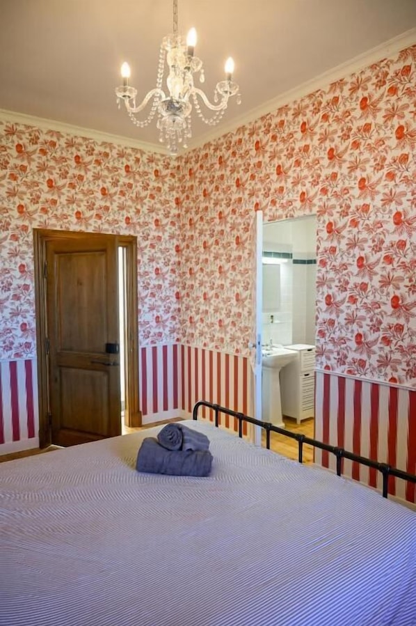 A bedroom with a bed, a chandelier, a wooden door, and a mirror.