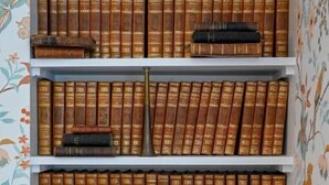 A bookshelf with multiple rows of books, some with spines facing outward and others stacked. - Château de Saint Clair (Saint-Clair-sur-l'Elle)