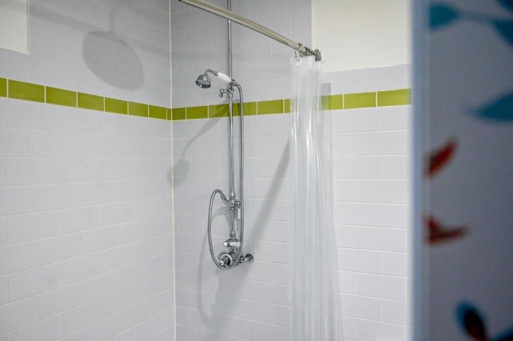 A shower area with a glass door, a showerhead, and a handrail.