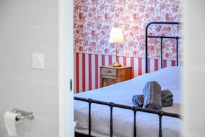 Ein Schlafzimmer mit einem Bett, einem Nachttisch, einer Lampe und einer Wand mit Blumenmuster-Tapete.