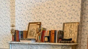 A room with a fireplace, a door, and a patterned wallpaper. - Château de Saint Clair (Saint-Clair-sur-l'Elle)