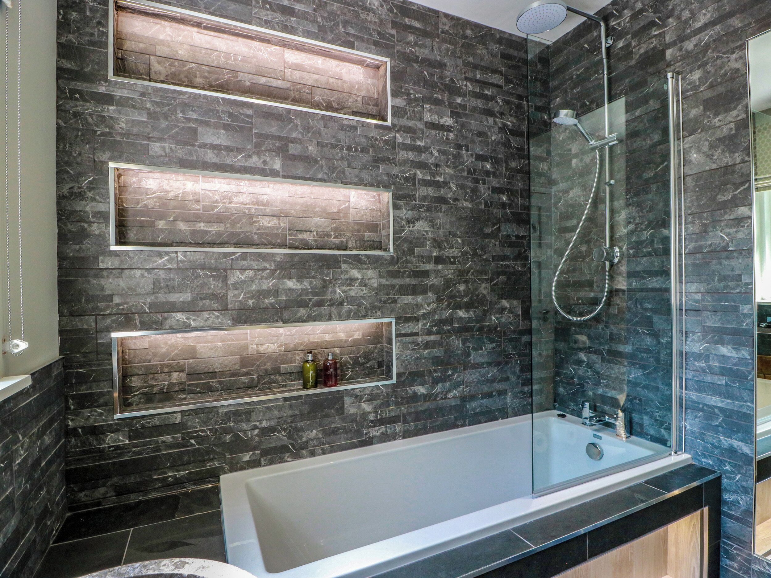 Un baño moderno con ducha envuelta en vidrio, una bañera independiente y estantes empotrados con artículos de aseo.