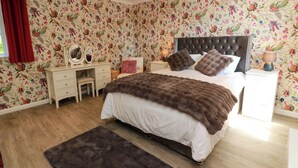 Un dormitorio con cama, cómoda, mesita de noche, espejo y papel tapiz con motivos florales.