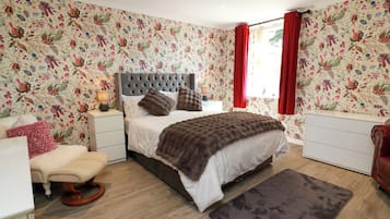 A bedroom with a tufted headboard, a bed with a brown blanket, a bedside table with a lamp, a chair, and a dresser.