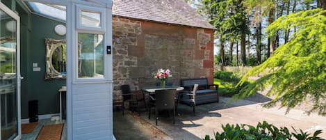 A cozy outdoor seating area with a stone wall, a door leading to a room, and lush greenery.