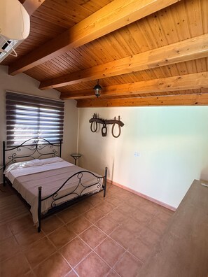 A bedroom with a bed, wooden ceiling beams, a wall-mounted light fixture, and a window with blinds. - Cal Piano Vacation Home with Private Pool, Wi-Fi, and Air Conditioning (Palol de Revardit)