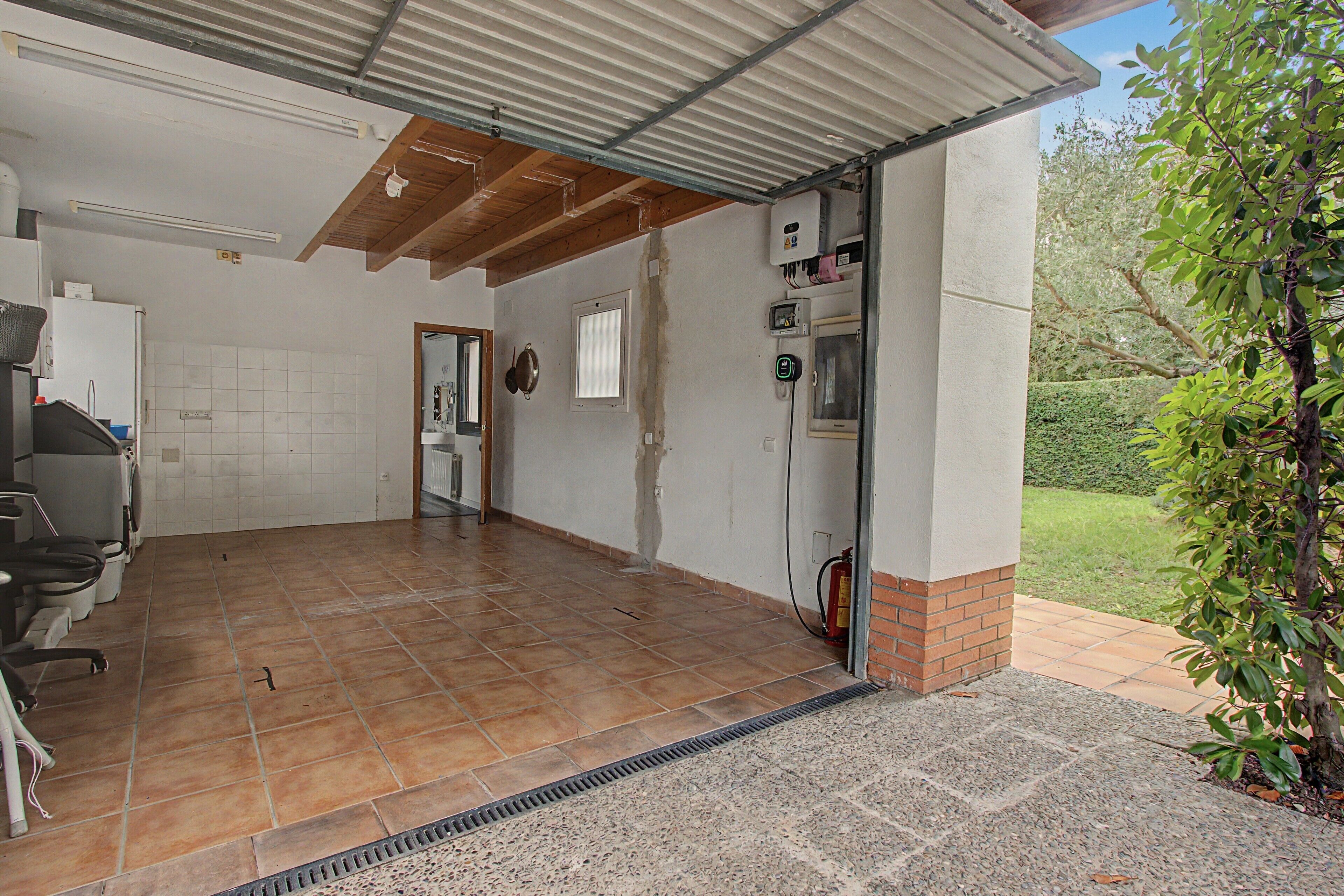 A covered outdoor area with a tiled floor, a fire extinguisher, and a hose on the right side.