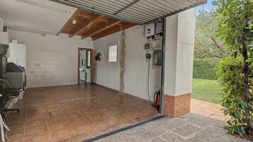 A covered outdoor area with a tiled floor, a fire extinguisher, and a hose on the right side.