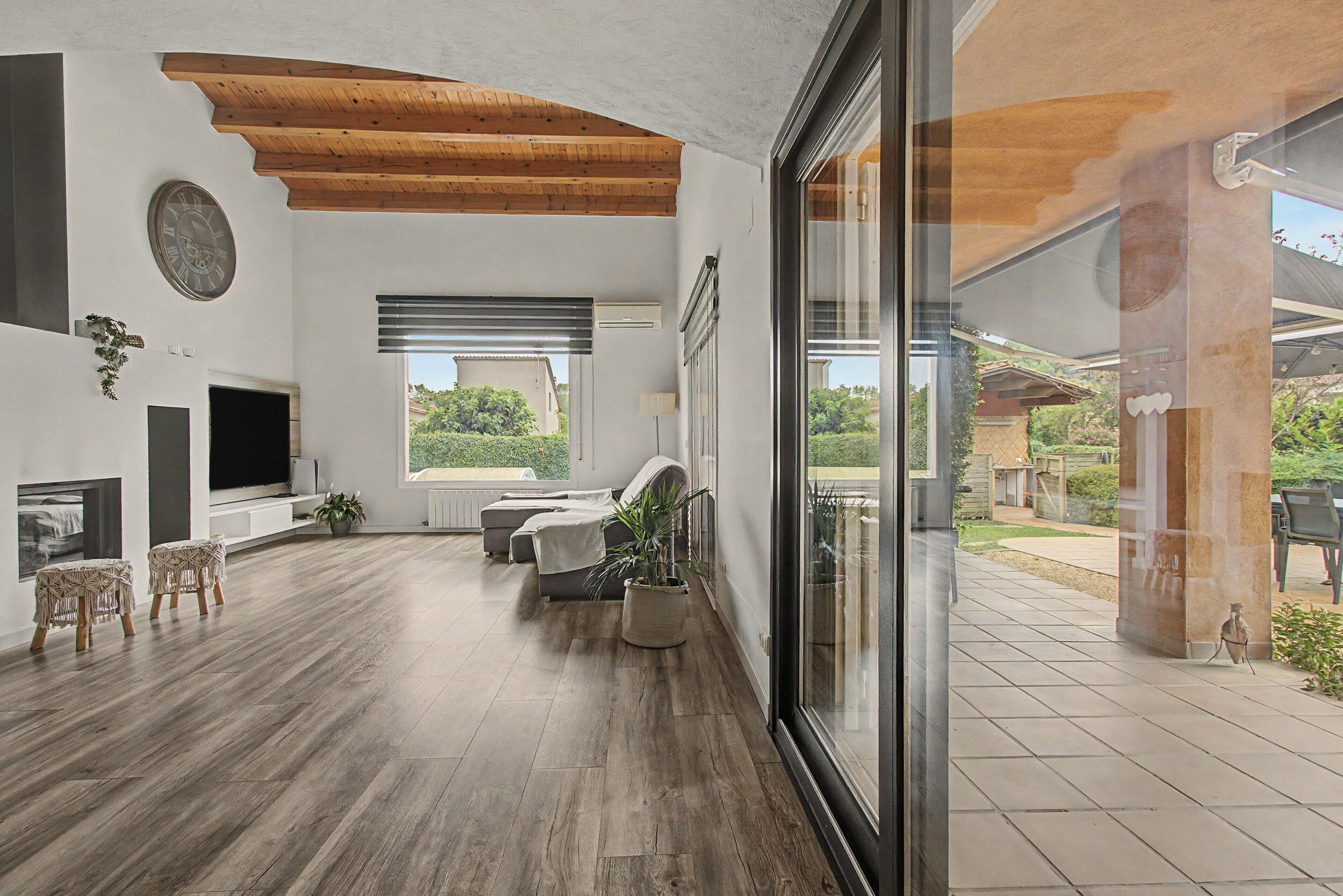 A spacious living room with a wooden ceiling, a large window, and a view of the outdoors.