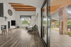 A spacious living room with a wooden ceiling, a large window, and a view of the outdoors. - Cal Piano Vacation Home with Private Pool, Wi-Fi, and Air Conditioning (Palol de Revardit)