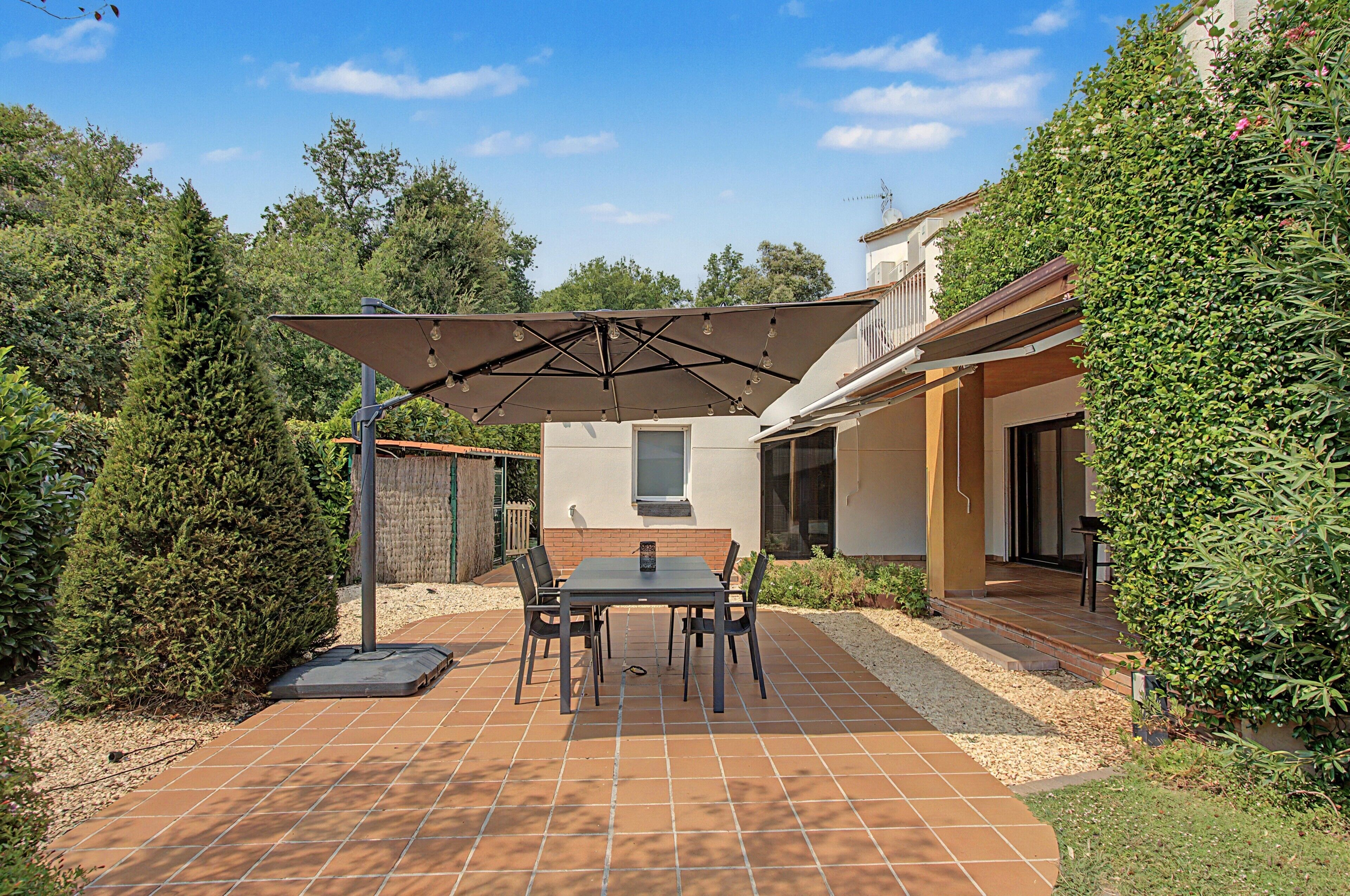 A patio with a table and chairs, surrounded by a garden and a building.