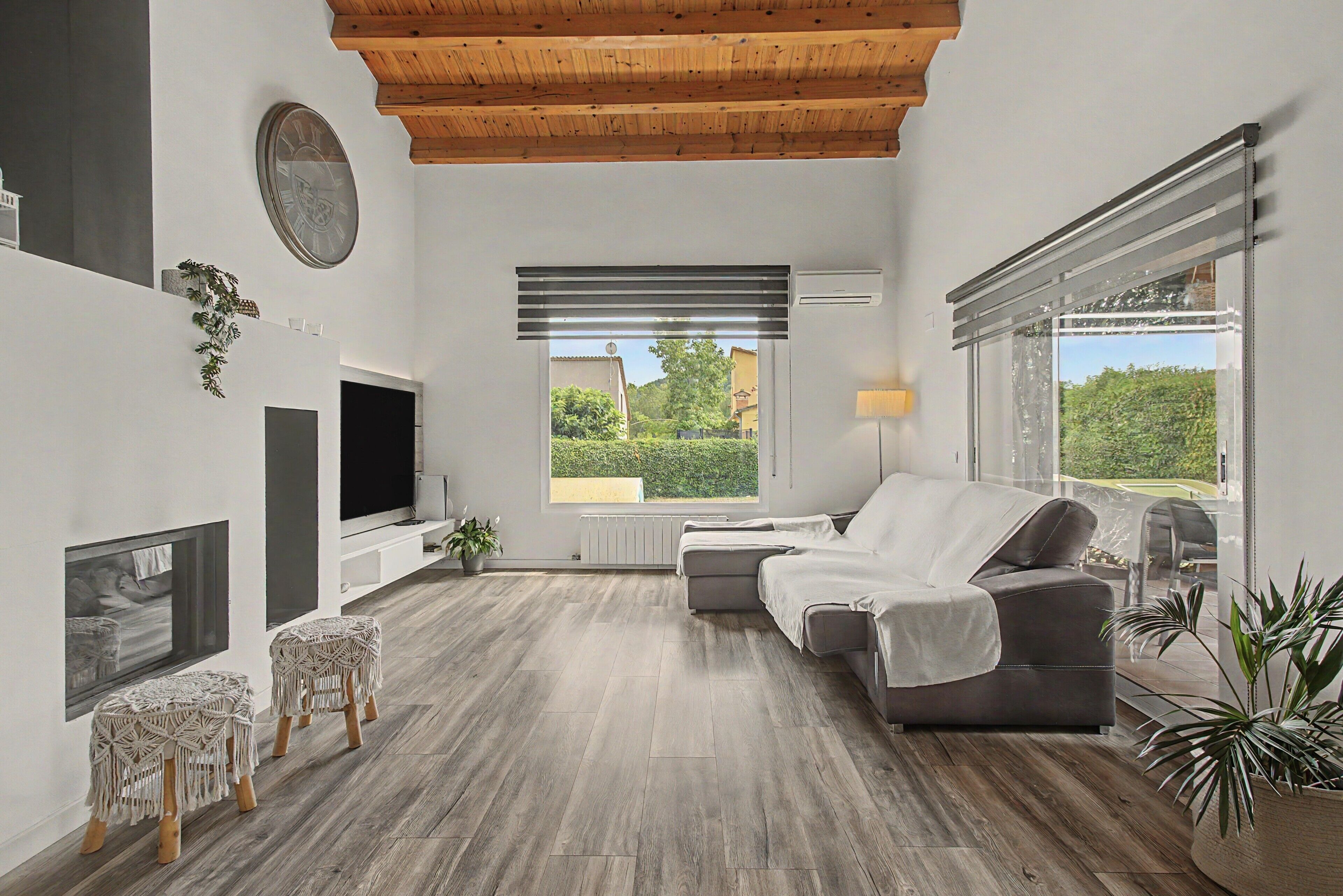 A modern living room with a fireplace, a flat-screen TV, a sofa, and a large window offering a view of greenery.