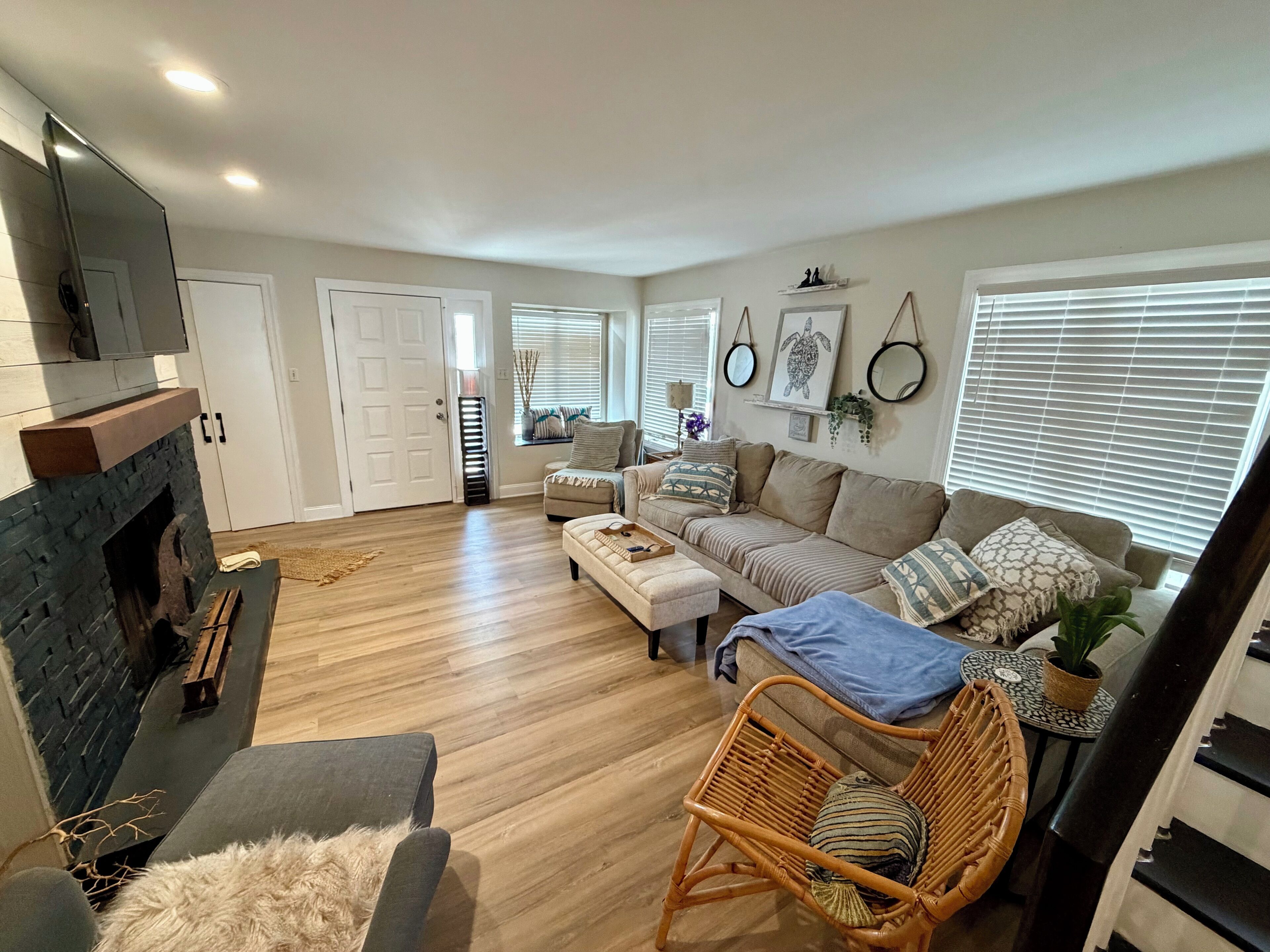 A spacious living room with a fireplace, a sofa set, a wicker chair, and a small table with a plant.