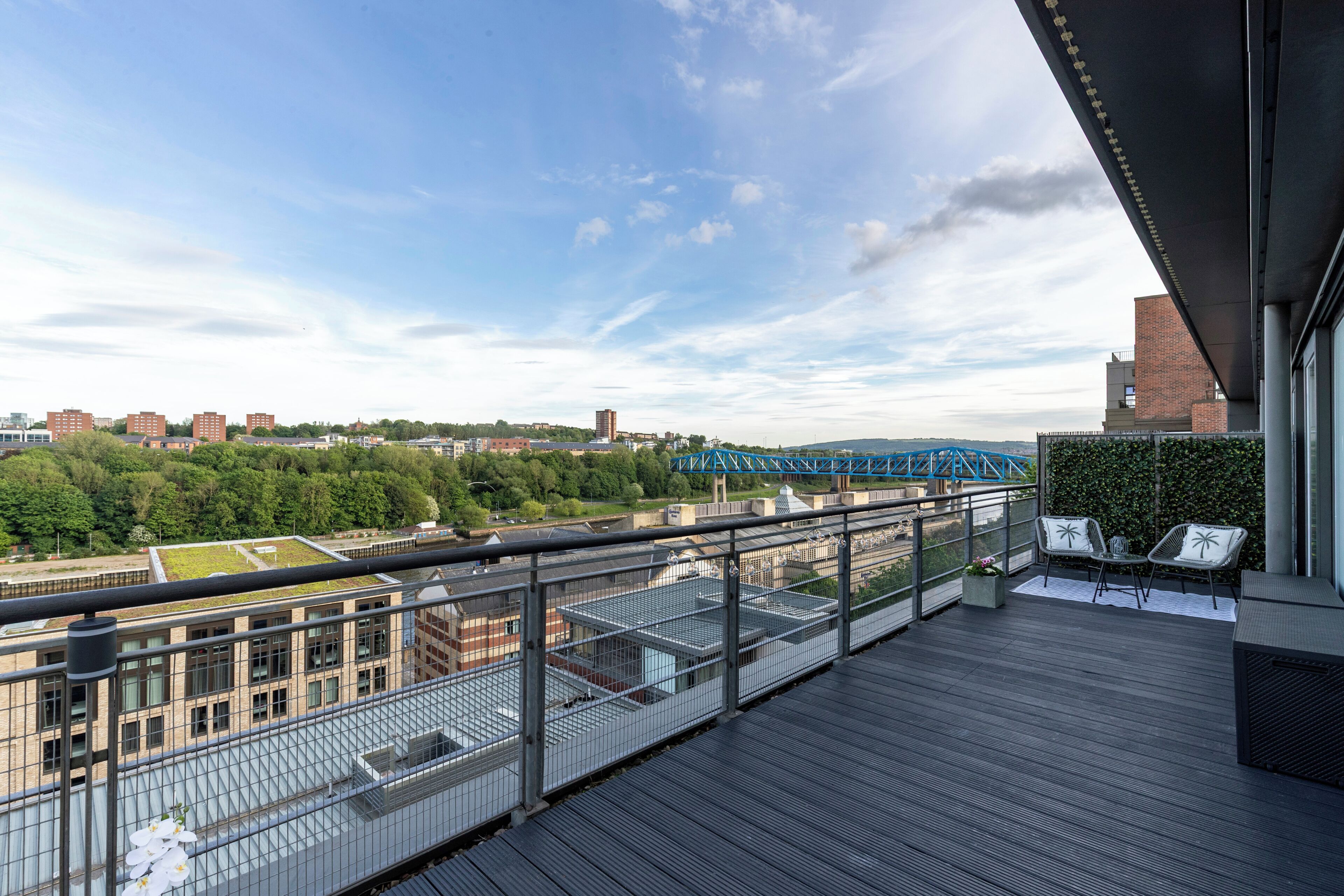 A balcony with a view of a cityscape, including a bridge, buildings, and greenery.
