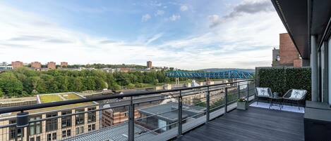 A balcony with a view of a cityscape, including a bridge, buildings, and greenery.