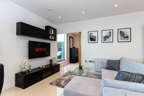 Ein modernes Wohnzimmer mit Flachbildfernseher, einer Couch, einem Couchtisch und Kunstwerken an der Wand.