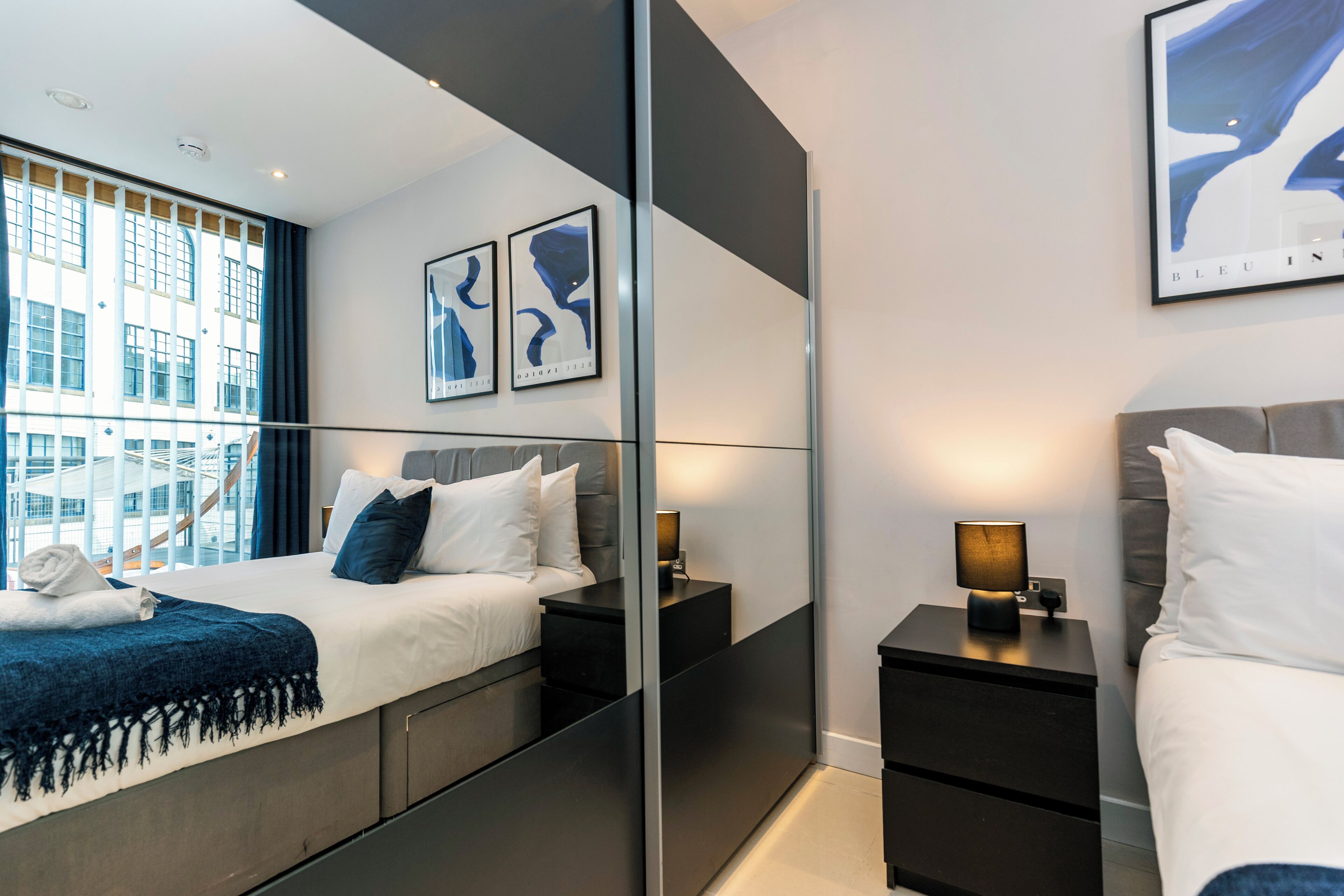 A modern hotel room with a large bed, bedside tables, a mirror, and artwork on the walls.