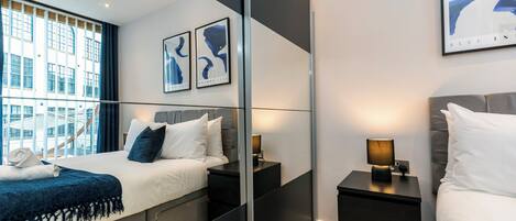 A modern hotel room with a large bed, bedside tables, a mirror, and artwork on the walls.