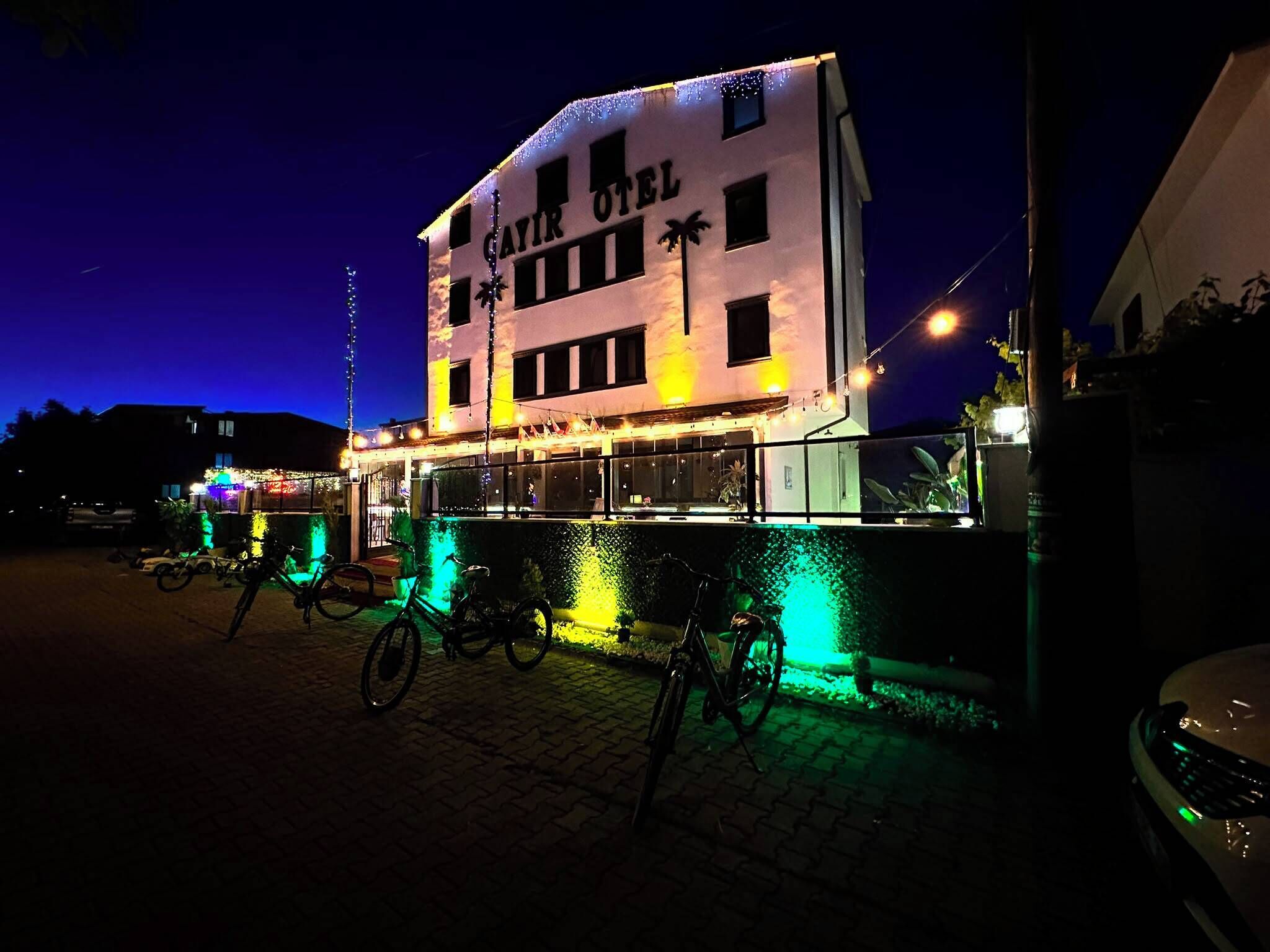 Ein Gebäude mit der Aufschrift 'SAIR OTEL' bei Nacht, mit einem Balkon, der Fahrräder und Lichterketten zeigt.