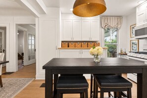 A modern kitchen with white cabinetry, a dark wooden table, and a hanging light fixture.