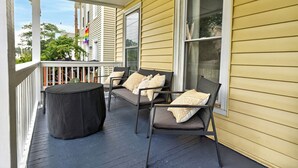 A covered porch with two chairs and a table, a railing, and a window.