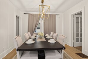 Een eetkamer met een donker houten tafel gedekt voor zes personen, beigekleurde fauteuils, een kroonluchter en uitzicht op een trap.