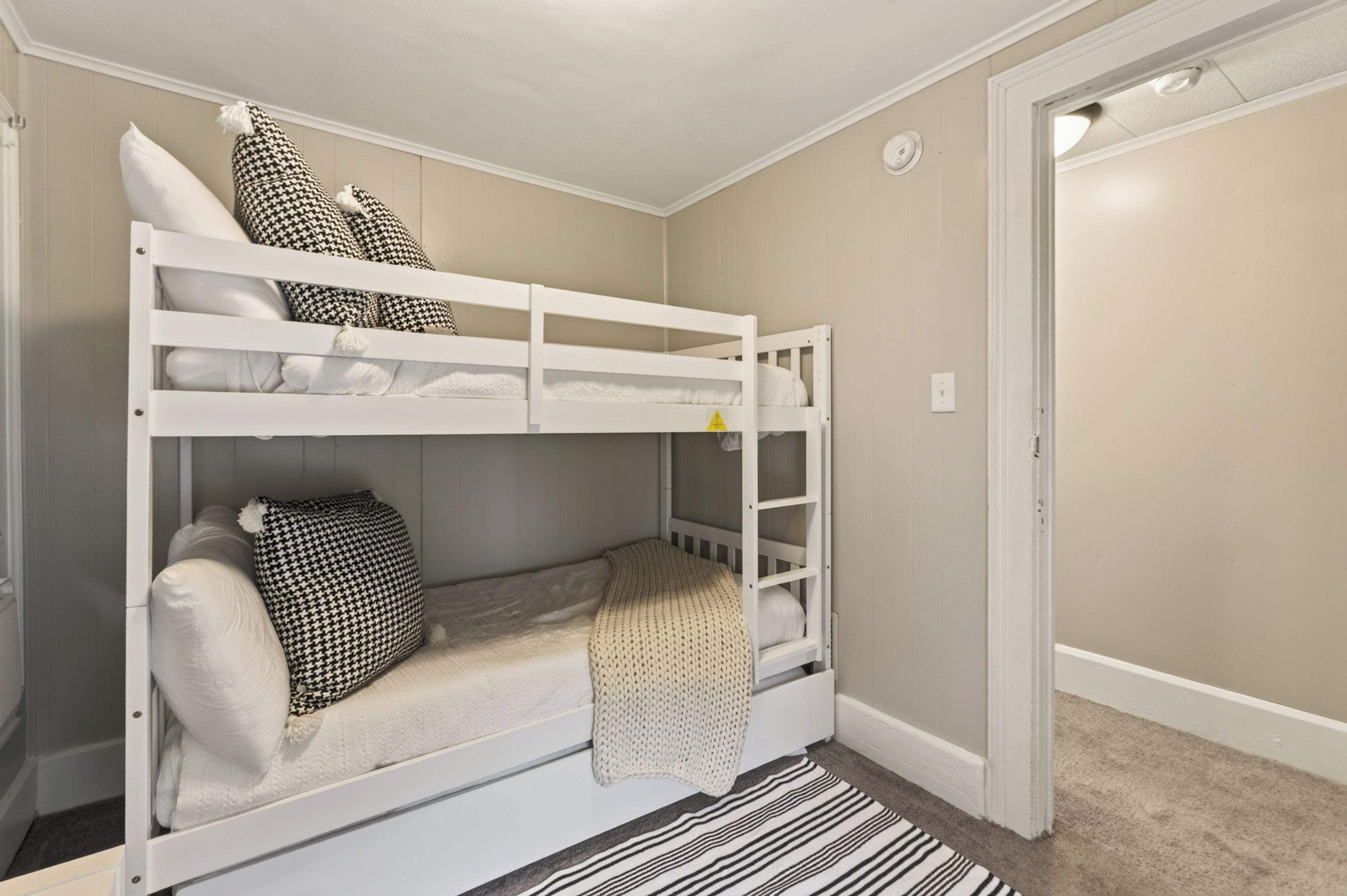 A bunk bed with a white frame, a striped rug, and a door to the right.