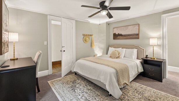 A bedroom with a bed, bedside tables, a desk, a chair, a ceiling fan, and a rug.