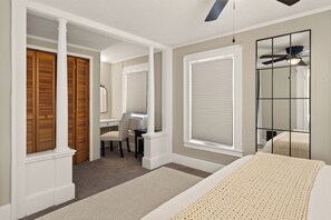 A bedroom with a bed, a desk, and a chair. There are two windows with blinds.