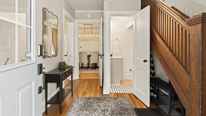 A hallway with a wooden staircase, a mirror, a desk, and a chandelier.
