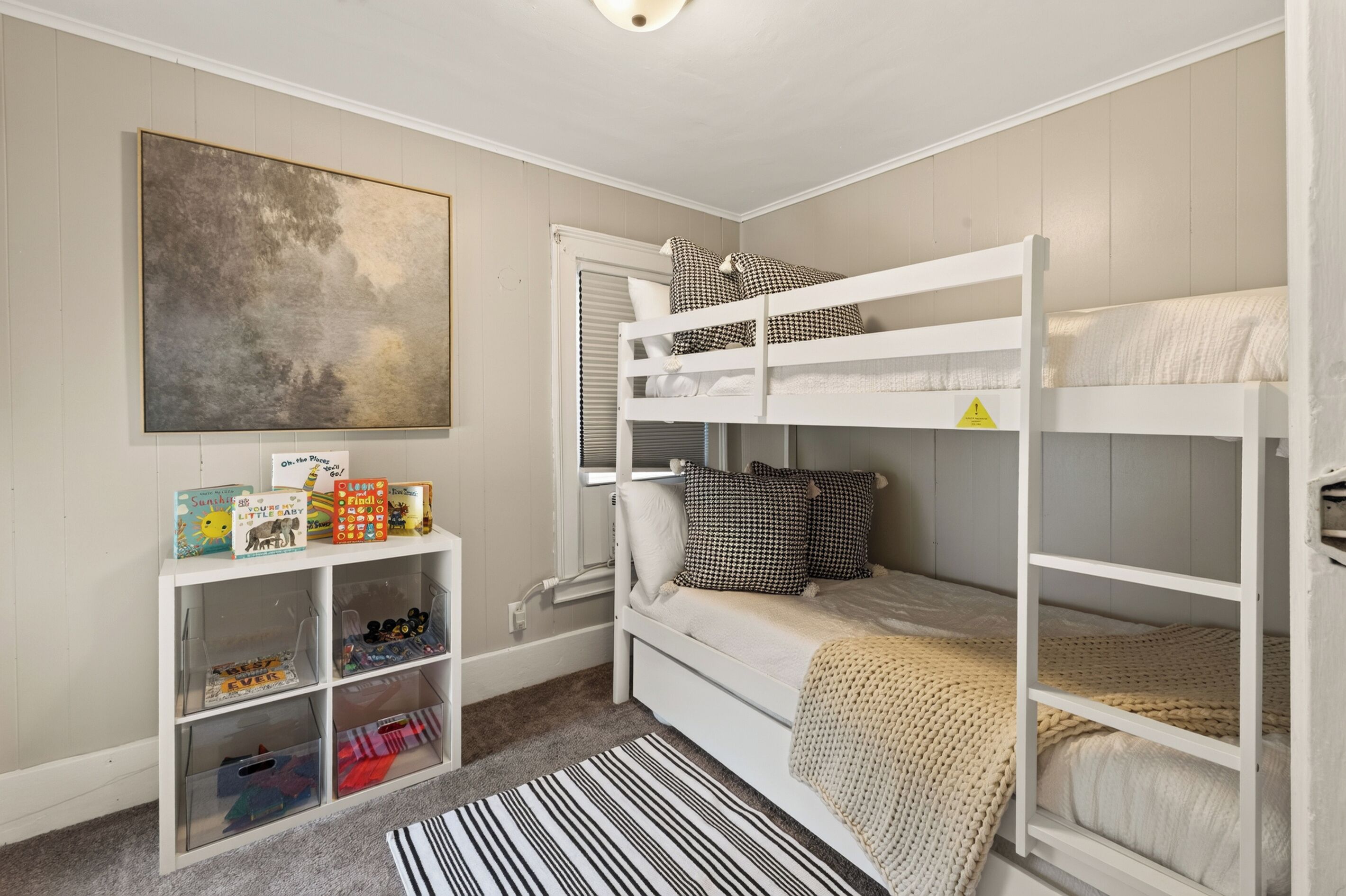 A child's bedroom with bunk beds, a bookshelf, and a large abstract painting.