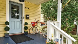 A yellow house with a blue door, a porch with a white railing, a bicycle, and a mailbox.