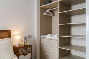 Ein Schlafzimmer mit Bett, Nachttisch, Lampe und begehbarem Kleiderschrank mit Regalen und Platz zum Aufhängen.