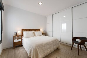 Un dormitori amb llit, taules de nit, una cadira i un armari.