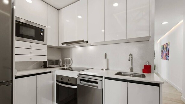 A modern kitchen with white cabinetry, a built-in microwave, a toaster, a coffee maker, a dishwasher, and a sink with a faucet. - Old Town Estepona Penthouse (Estepona)