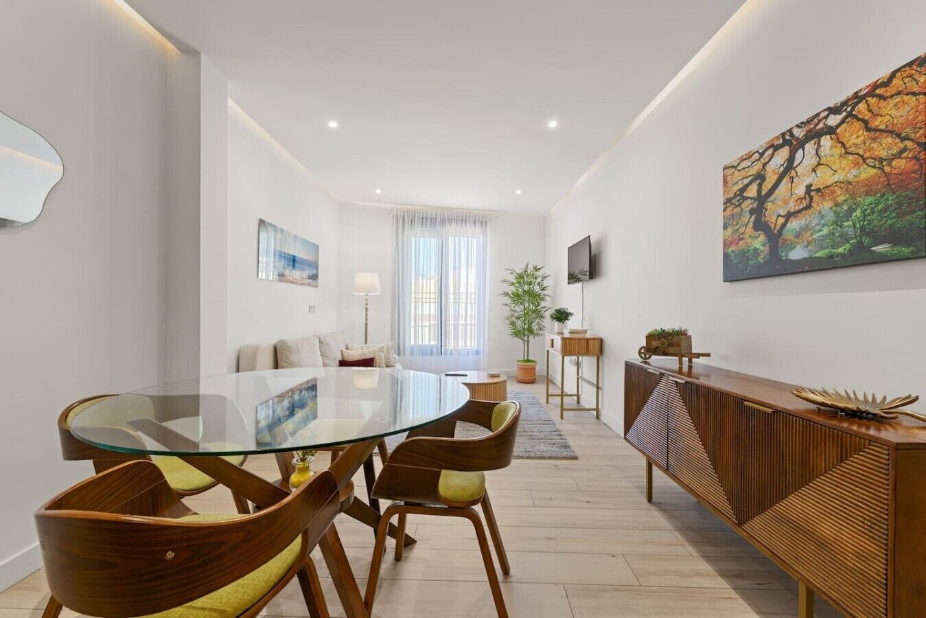 A modern dining area with a glass table, wooden chairs, and a wooden sideboard.