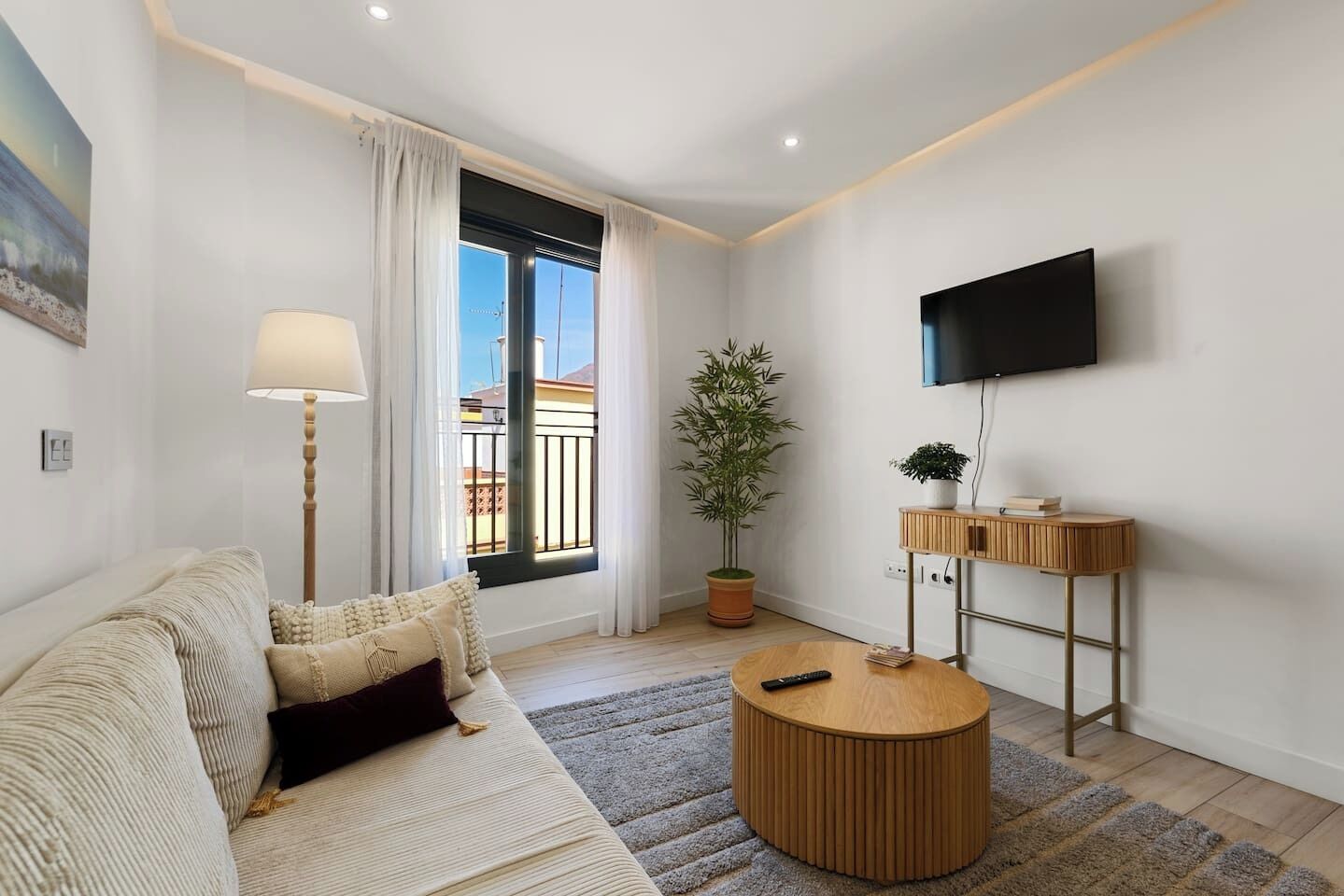 Una sala de estar moderna con un sofá, una mesa de centro redonda, una lámpara de pie, una planta en maceta y un televisor de pantalla plana montado en la pared.