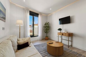 Ein modernes Wohnzimmer mit einer Couch, einem runden Couchtisch, einer Stehlampe, einem Blumentopf und einem an der Wand befestigten Flachbildfernseher.