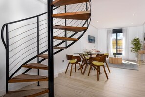 Ein modernes Interieur mit einer Wendeltreppe, einem Essbereich mit Holzsesseln und einem großen Fenster, das für natürliches Licht sorgt.