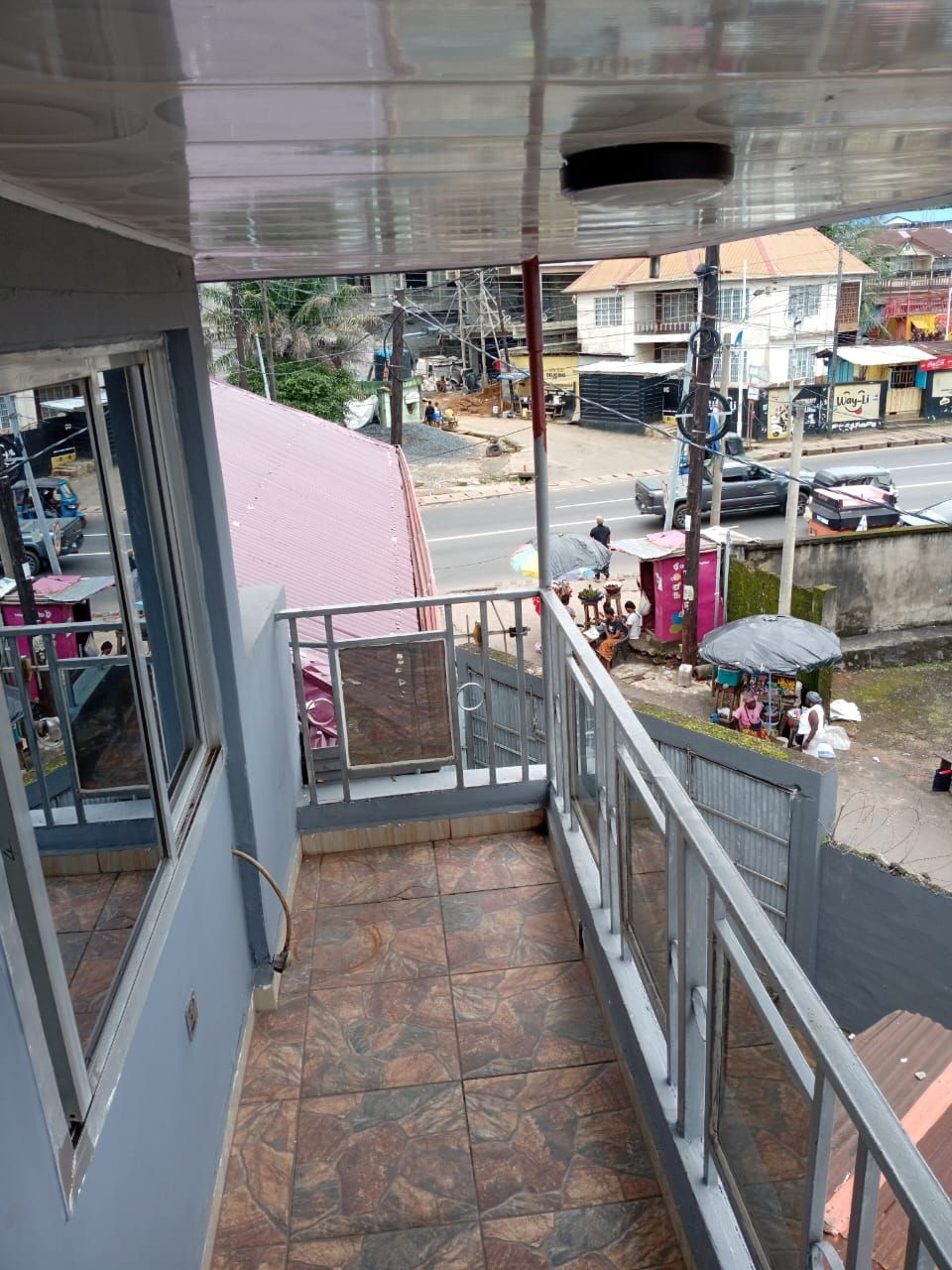 Een balkon met een metalen hekwerk, met uitzicht op een straat vol winkels en verkeer.